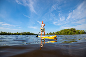 Joyful man paddling on a SUP board on large river