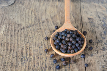 Dried black pepper corns on wooden spoon.