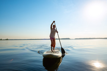 Joyful man is training on a SUP board on a large river