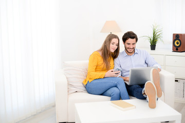 cheerful young couple on sofa at home websurfing and shopping online with laptop computer internet technology