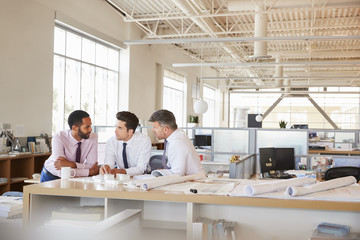 Three male architects in discussion in an open plan office