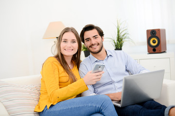 cheerful young couple on sofa at home websurfing and shopping online with laptop computer internet technology