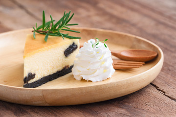 Delicious and sweet original plain New York cheesecake on wooden plate served with whipped cream on wood table with copy space in side view. Homemade bakery for cafe and restaurant or birthday cake.