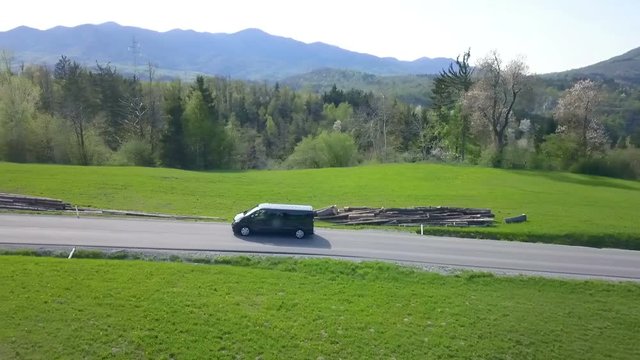 A black van is slowly driving on the road in the countryside. Aerial shot.