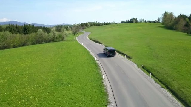 Gorgeous green countryside. The day is beautiful. Aerial shot. A van is driving on the road.