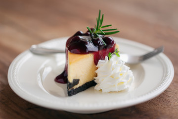 Delicious and sweet blueberry New York cheesecake on white plate served with whipped cream on wood table in side view with copy space. Homemade bakery for cafe and restaurant or birthday cake.