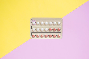 Oral contraceptive pills blister on yellow pink background. Hormones used to prevent pregnancy and...