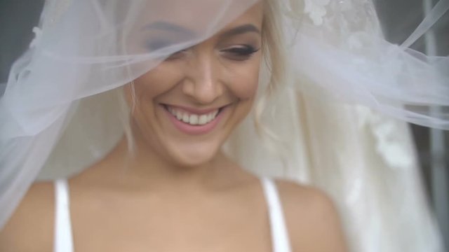 Charming attractive blonde bride with pretty smile and make-up is posing under the veil. Close up portrait.