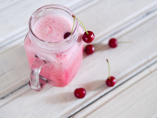 Cherry smoothies with fresh cherries on a wooden table.
