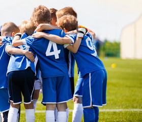 Boys sports team with coach. Youth soccer team huddle with coach. Motivation talk, pep talk before the match. Young football soccer players in jersey blue sportswear