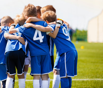 Boys sports team with coach. Youth soccer team huddle with coach. Motivation talk, pep talk before the match. Young football soccer players in jersey blue sportswear © matimix