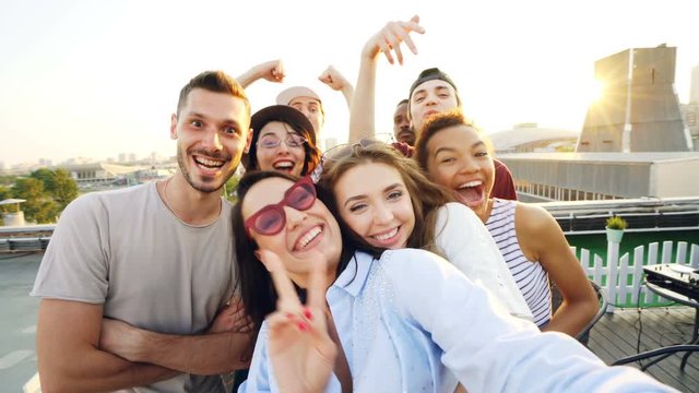 Point of view shot of happy friends taking selfe on roof at summer party laughing, posing and enjoying good company. Happiness, leisure and technology concept.
