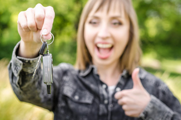 Young smilling happy woman with car key closeup on green nature background auto concept
