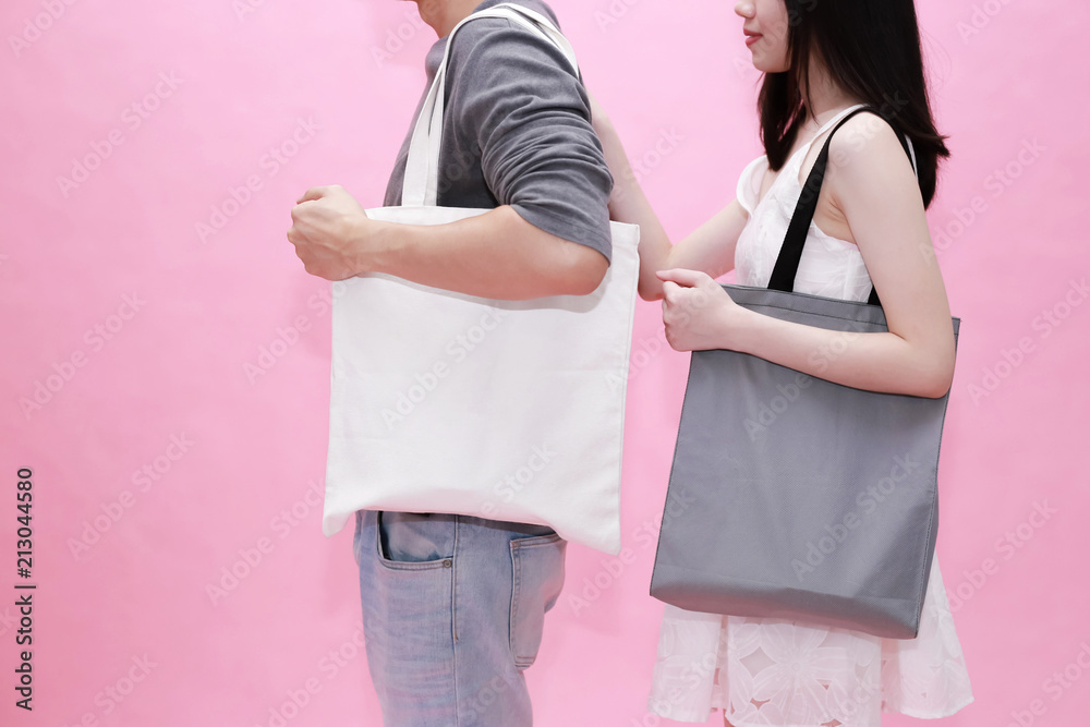 Wall mural Young male and female couple using an empty blank tote cotton bag together in pink background - with copy space to insert anything.