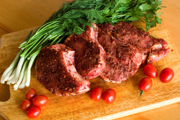 meat with red pepper on a wooden chopping board with onions, dill and tomatoes