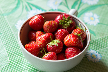ripe strawberry berry with green leafs in a plate on a green background