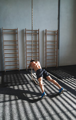 Fit young man in gym working out with climbing rope.