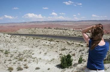 Naklejka premium Young woman seen from the back looking out on an deserted highway in the desert