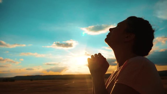 girl praying. girl folded her hands in prayer silhouette at sunset. slow motion video. Girl folded her hands in prayer pray to God. asks lifestyle forgiveness for sins of repentance. believing girl