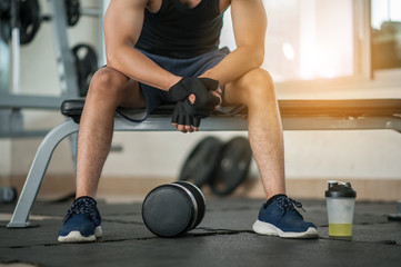 Muscular man at gym taking a break from workout sitting side mineral salt.Body and mind workout in loft fitness studio.Closeup on fitness man taking dumbbell from the floor in urban loft gym