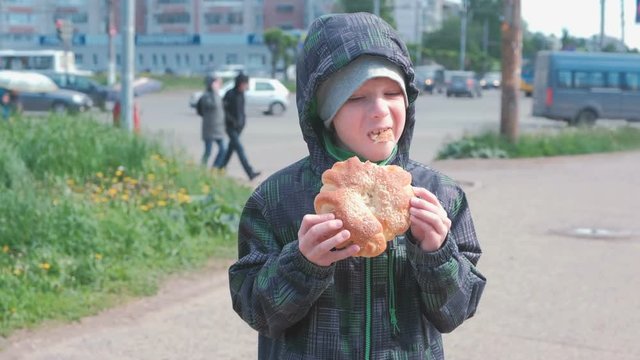 Boy eating a bun on the street.