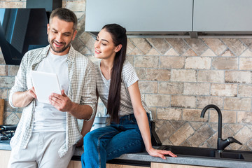 portrait of smiling couple using digital tablet together in kitchen, smart home concept