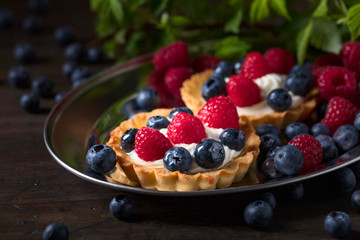  Dessert tarts with raspberries and blueberries on a wooden table.