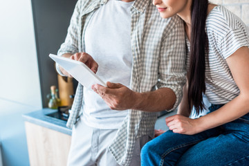cropped shot of married couple using digital tablet together in kitchen, smart home concept