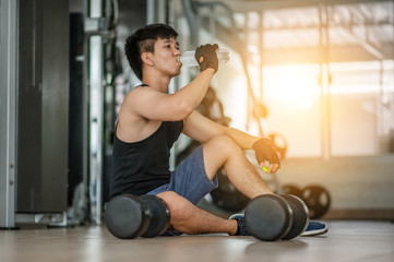 Fototapeta na wymiar Handsome young man drinking water from a bottle and taking a break from exercising in a gym