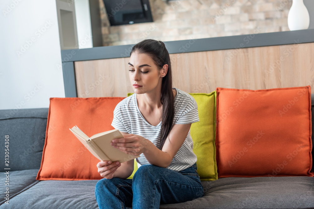 Wall mural portrait of attractive woman reading book on couch at home