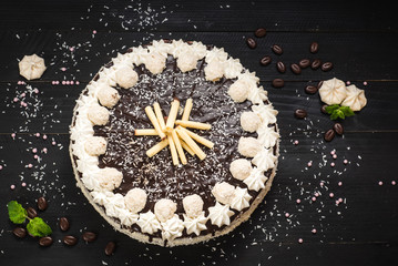 Sweet white cake with chocolate and meringue on the black wooden background