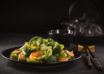 Hot stir fried vegetables on black plate. Healthy asian food concept with copy space. Toned