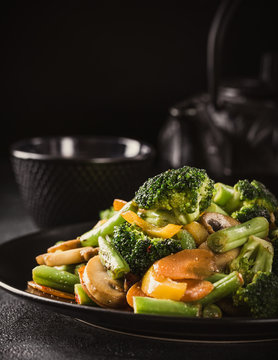 Hot stir fried vegetables on black plate. Healthy asian food concept with copy space. Toned