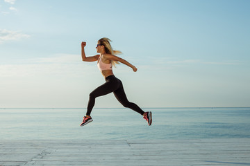 Young woman with fit body jumping and running against blue sea