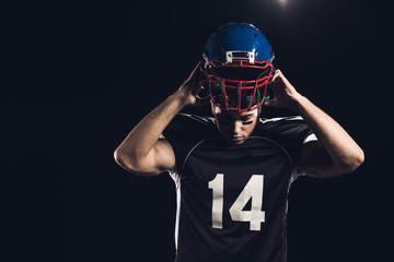young american football player putting on helmet isolated on black