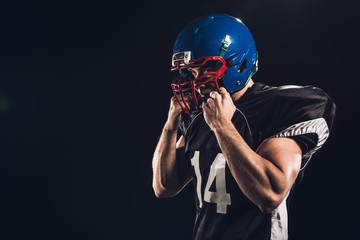 american football player putting on helmet isolated on black