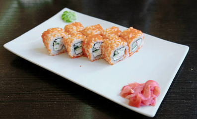 Rolls with caviar with pickled ginger and wasabi on a white rectangular plate.