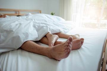 Obraz na płótnie Canvas Love lying in bed in hotel,embracing on white sheets, close up legs.