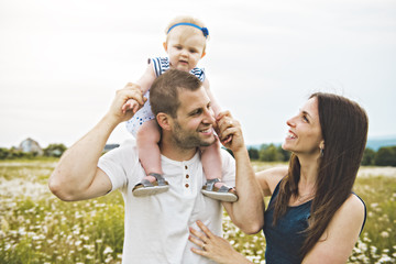 littlegirl and his father and mother enjoying outdoors in field of daisy flowers