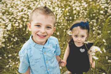 Fototapeta na wymiar Two cute childs playing in green daisy field