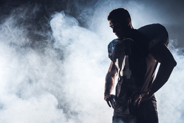 dark silhouette of thoughtful american football player looking down against white smoke