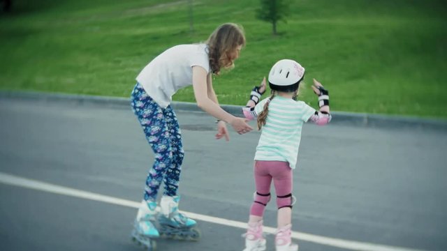 Mother helps her daughter to skate in a roller-skating park