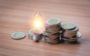 Energy saving light bulb and tree growing on stacks of coins on nature background. Saving, accounting and financial concept.