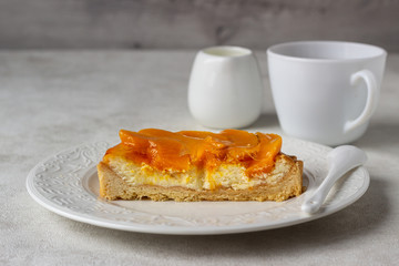 Cheesecake with apricots and jelly topping on a white plate and light background. 