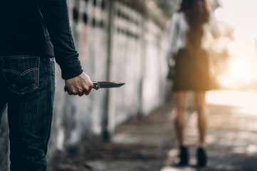 A bandit holds a knife. In order to attack and steal a woman's belongings from the back.