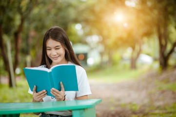 Fototapeta premium Asian girl reading book at park in summer sunset light. asian woman reading book in Thailand. asian Beautiful woman reading a book at table.