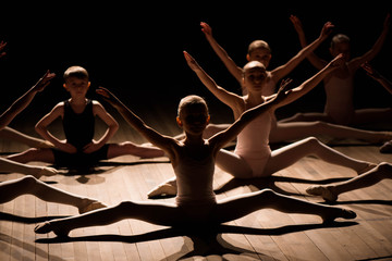 Obraz premium Pretty young girl and boy sitting on stage having stretching and training for ballet dances.