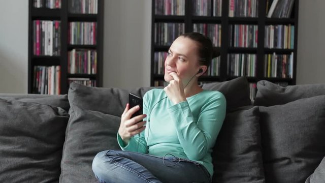 Woman on the sofa at home playing music with her smarphone and wearing headphones