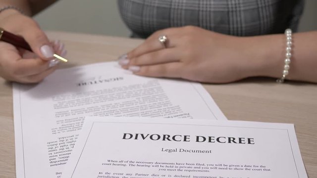 Divorce Decree legal document being signed by a woman sitting at a desk.