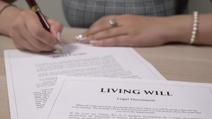 Living Will legal document being signed by a woman sitting at a desk.